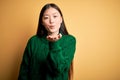 Young beautiful asian woman wearing green winter sweater over yellow isolated background looking at the camera blowing a kiss with Royalty Free Stock Photo