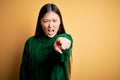 Young beautiful asian woman wearing green winter sweater over yellow isolated background pointing displeased and frustrated to the