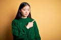 Young beautiful asian woman wearing green winter sweater over yellow isolated background Pointing with hand finger to the side