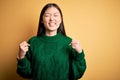 Young beautiful asian woman wearing green winter sweater over yellow isolated background very happy and excited doing winner Royalty Free Stock Photo
