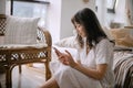 Young beautiful asian woman in white summer dress using smartphone while relaxing at home Royalty Free Stock Photo