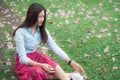 Young beautiful asian woman  wore denim shirt and red skirt sitting in a garden filled with falling pink  flowers Royalty Free Stock Photo