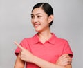 Young beautiful asian woman wore pink t shirt,smile and Pointing with confidence Showed smart expression , on gray background