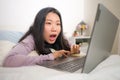 Young beautiful Asian woman working with laptop on bed -  lifestyle home portrait of young pretty and happy Japanese student girl Royalty Free Stock Photo