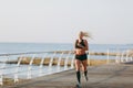 Young beautiful athletic girl with long blond hair in black clothes running at sunrise over the sea Royalty Free Stock Photo