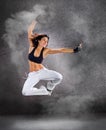 Young beautiful athletic woman jumping dancing modern style dance hip-hop on studio on wall background with smoke Royalty Free Stock Photo