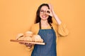 Young beautiful baker woman with blue eyes wearing apron holding tray with bread with happy face smiling doing ok sign with hand Royalty Free Stock Photo