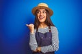 Young beautiful baker woman wearing apron and hat standing over isolated blue background smiling with happy face looking and Royalty Free Stock Photo