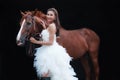 Young beautiful beauty bride in fashion white bridal wedding costume stand by handsome horse on black background Royalty Free Stock Photo