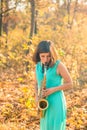 Beautiful young girl with black hair and a tattoo on her arm, dressed in a long blue dress and plays the alto saxophone in autumn Royalty Free Stock Photo