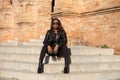 young and beautiful black latin woman wearing black clothes and sunglasses is sitting on the steps of the most important square in