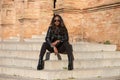 young and beautiful black latin woman wearing black clothes and sunglasses is sitting on the steps of the most important square in