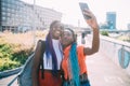 Young beautiful black sisters outdoor backlight using smartphone taking selfie