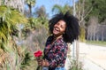 Young, beautiful black woman with afro hair holds a red flower in her hands. The beautiful woman is happy and smiling Royalty Free Stock Photo