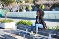 Young, beautiful, black woman with afro hair, wearing a jacket, jeans and boots, sitting on a bench, self-confident, happy and