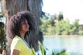 Young, beautiful black woman with afro hair wearing jeans and yellow shirt looking at the river from the shore. The woman is happy Royalty Free Stock Photo