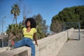 Young, beautiful, black woman with afro hair, wearing a yellow t-shirt, jeans and boots, sitting on a stone wall, relaxed and calm Royalty Free Stock Photo