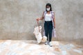 Young beautiful woman wearing disposable medical face mask playing with Beagle dog in the park during coronavirus outbreak.