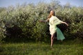 Young beautiful blond smiling woman in yellow transparent cloth jumping on grass over blooming cherry trees background Royalty Free Stock Photo