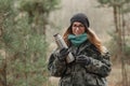 Young beautiful blond woman in camouflage outfit and green scarf posing with thermos in the forest. Travel lifestyle concept.