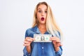 Young beautiful blond woman holding dollar standing over isolated white background scared in shock with a surprise face, afraid Royalty Free Stock Photo