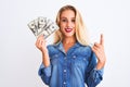 Young beautiful blond woman holding dollars standing over isolated white background surprised with an idea or question pointing Royalty Free Stock Photo