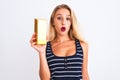 Young beautiful blond woman holding gold ingot standing over isolated white background scared in shock with a surprise face, Royalty Free Stock Photo