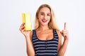 Young beautiful blond woman holding gold ingot standing over isolated white background surprised with an idea or question pointing Royalty Free Stock Photo