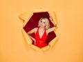 Young and beautiful blond woman in a red dress over yellow torn paper background. Fall, autumn sales, shopping and Royalty Free Stock Photo