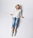 Young beautiful blond woman in stylish casual clothing, white sneakers and sunglasses sitting on floor and smiling, top view Royalty Free Stock Photo