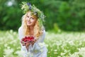 Young beautiful blond woman in white dress and floral wreath holding box of fresh strawberries on summer day Royalty Free Stock Photo