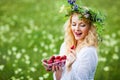 Young beautiful blond woman in white dress and floral wreath holding box of fresh strawberries on summer day Royalty Free Stock Photo