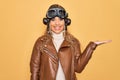 Young beautiful blonde aviator woman wearing vintage pilot helmet whit glasses and jacket smiling cheerful presenting and pointing Royalty Free Stock Photo