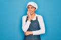 Young beautiful blonde baker woman with blue eyes cooking wearing apron and cap looking stressed and nervous with hands on mouth