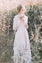 Young beautiful blonde bride wearing white dress with bouquet in blooming meadow. Delicate girl enjoys spring nature Royalty Free Stock Photo