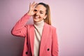 Young beautiful blonde businesswoman with blue eyes wearing elegant pink jacket doing ok gesture with hand smiling, eye looking Royalty Free Stock Photo