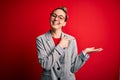 Young beautiful blonde businesswoman with blue eyes wearing glasses and jacket amazed and smiling to the camera while presenting Royalty Free Stock Photo