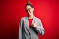 Young beautiful blonde businesswoman with blue eyes wearing glasses and jacket doing happy thumbs up gesture with hand Royalty Free Stock Photo