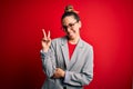 Young beautiful blonde businesswoman with blue eyes wearing glasses and jacket smiling with happy face winking at the camera doing Royalty Free Stock Photo