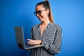 Young beautiful blonde businesswoman wearing glasses using laptop over blue background with a happy face standing and smiling with Royalty Free Stock Photo