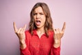 Young beautiful blonde casual girl over pink isolated background shouting with crazy expression doing rock symbol with hands up Royalty Free Stock Photo