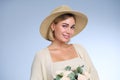 A young beautiful blonde caucasian woman with a short haircut in a beige suit and hat with bouquet of white flowers on Royalty Free Stock Photo