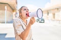 Young beautiful blonde caucasian woman smiling happy outdoors on a sunny day shouting through megaphone Royalty Free Stock Photo