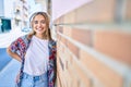 Young beautiful blonde caucasian woman smiling happy outdoors on a sunny day wearing headphones listening to music leaning on Royalty Free Stock Photo