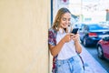 Young beautiful blonde caucasian woman smiling happy outdoors on a sunny day wearing headphones and using smartphone Royalty Free Stock Photo