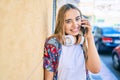 Young beautiful blonde caucasian woman smiling happy outdoors on a sunny day wearing headphones and using smartphone Royalty Free Stock Photo