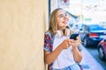 Young beautiful blonde caucasian woman smiling happy outdoors on a sunny day wearing headphones and using smartphone Royalty Free Stock Photo