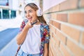 Young beautiful blonde caucasian woman smiling happy outdoors on a sunny day wearing headphones and using smartphone leaning on a Royalty Free Stock Photo