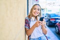 Young beautiful blonde caucasian woman smiling happy outdoors on a sunny day wearing headphones and using smartphone Royalty Free Stock Photo