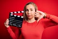 Young beautiful blonde clapper woman holding clapboard over isolated red background with angry face, negative sign showing dislike